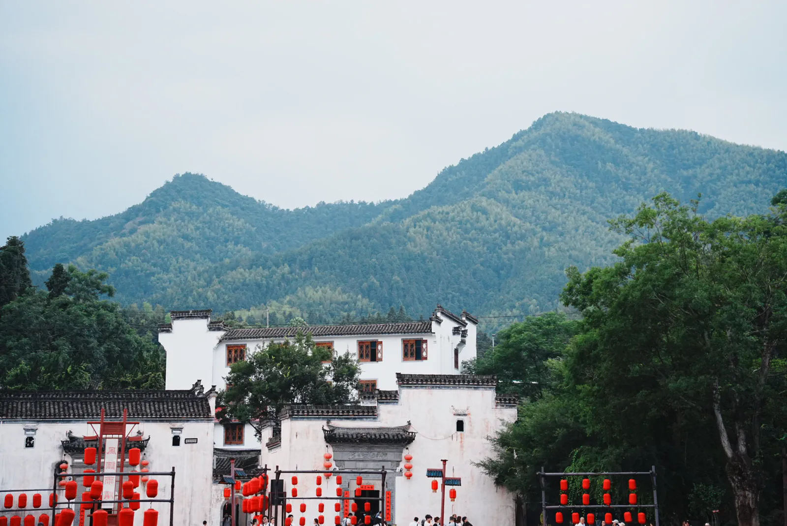 White village houses and red lanterns beneath misty green mountains.