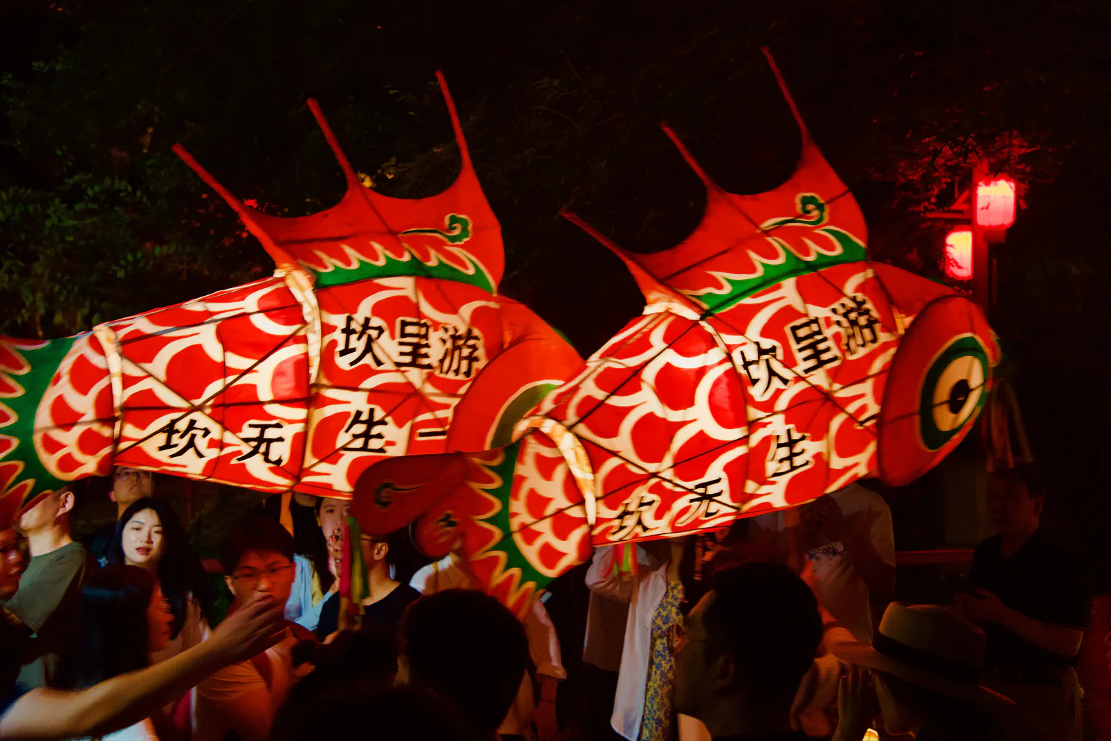 Two glowing red fish lanterns carried through a nighttime crowd.