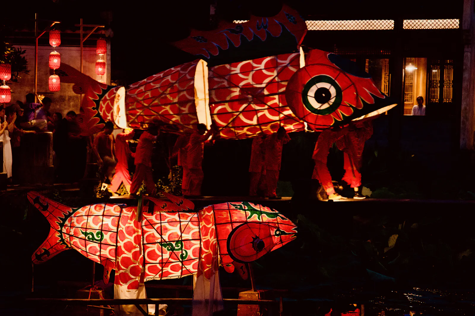 Illuminated fish lanterns reflected in the water at night.