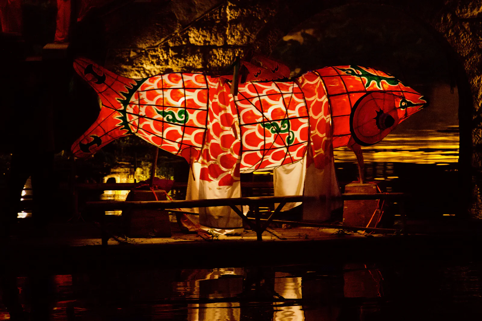 A bright red fish lantern against a dark stone bridge.