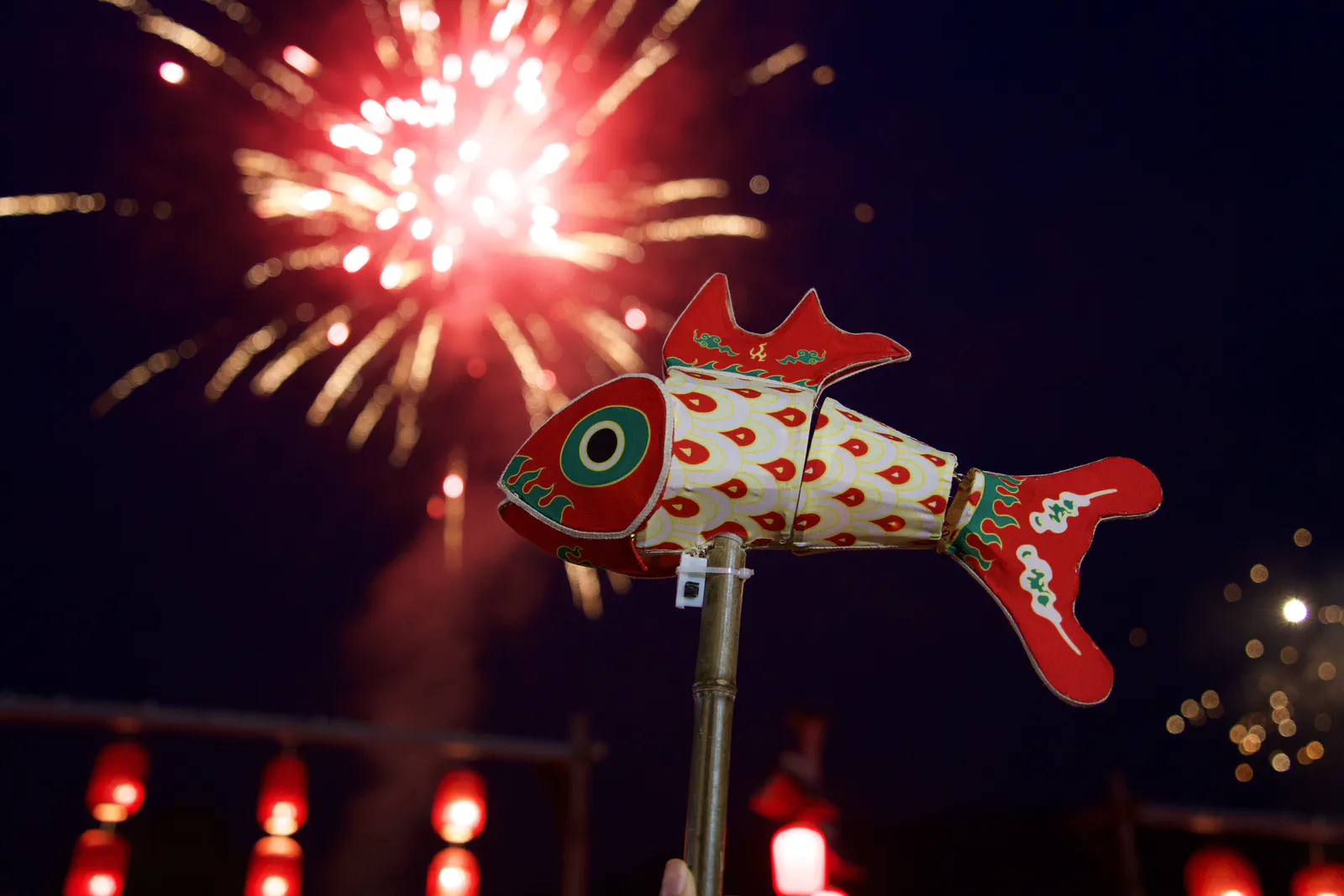 A small fish lantern held beneath a burst of fireworks.