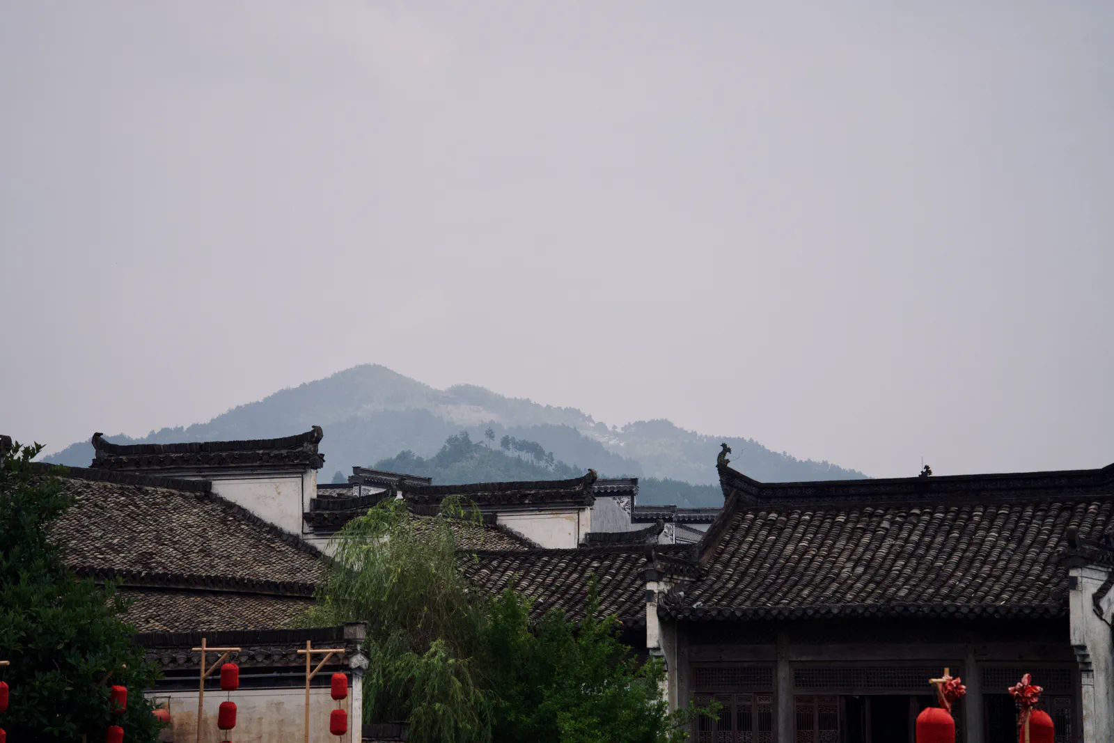 Dark village rooftops beneath layers of pale misty mountains.