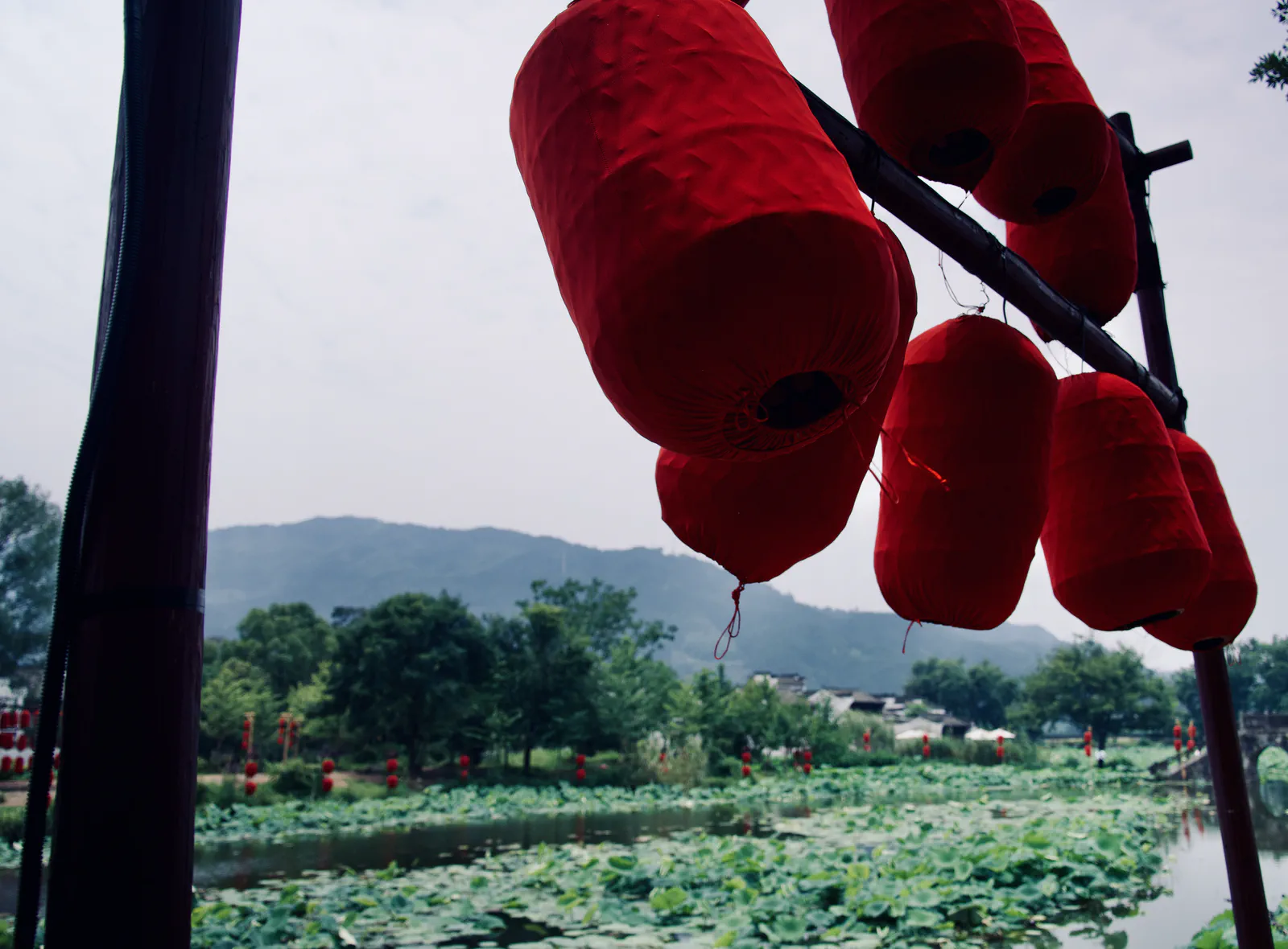 Red lanterns overlooking a lotus pond and distant green hills.
