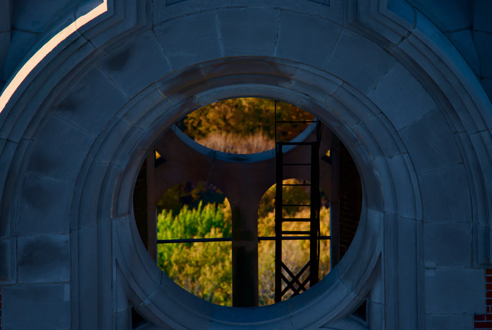 Autumn foliage seen through a circular opening in a stone church tower.