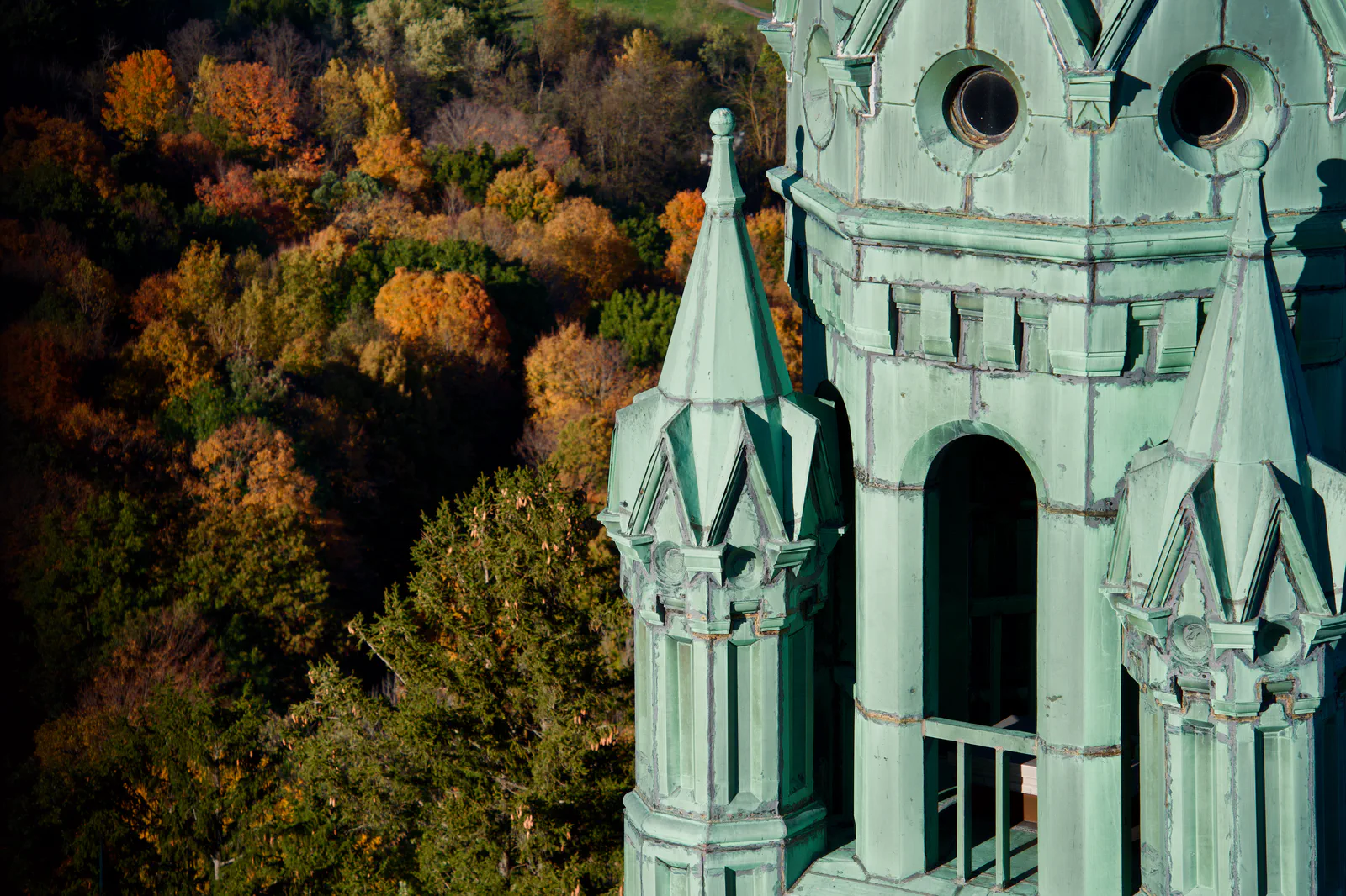 A close view of the green church tower with autumn woodland behind it.
