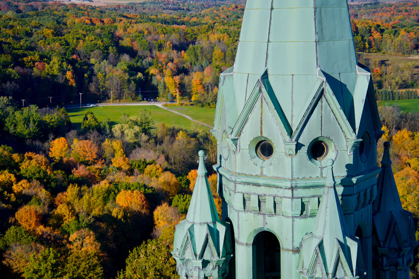 The green Holy Hill tower overlooking red, orange, and yellow autumn trees.