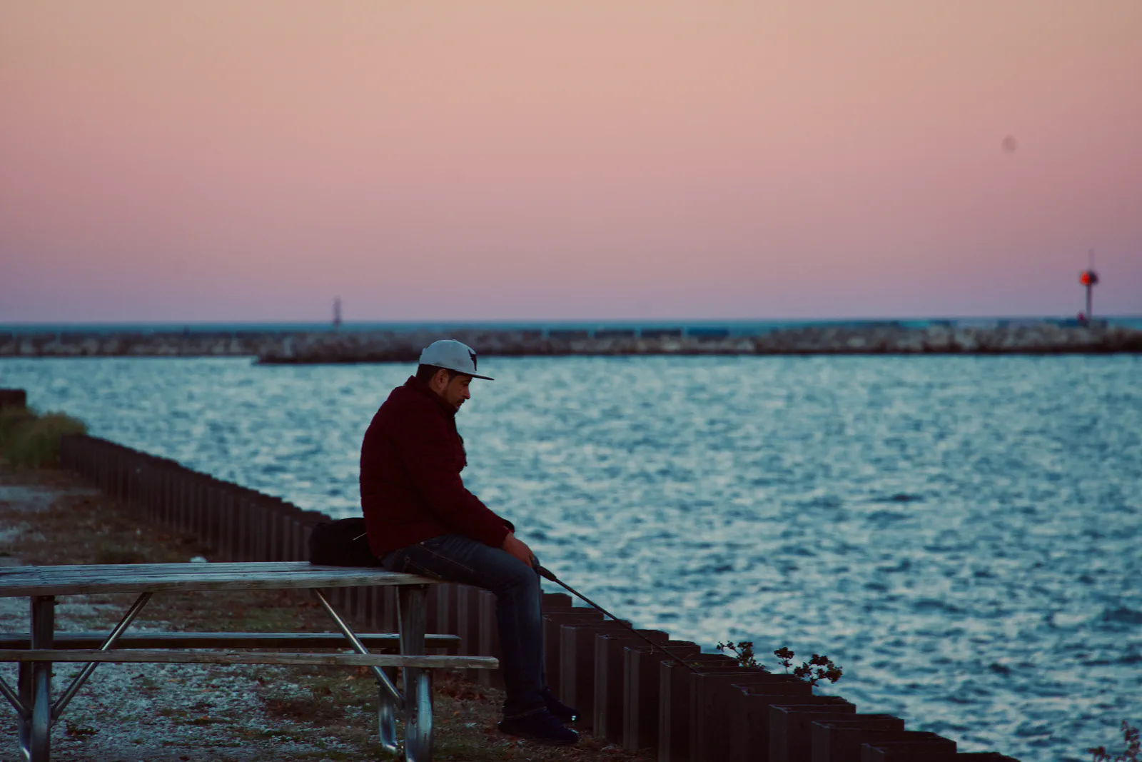 A person seated beside the lake beneath a pink evening sky.