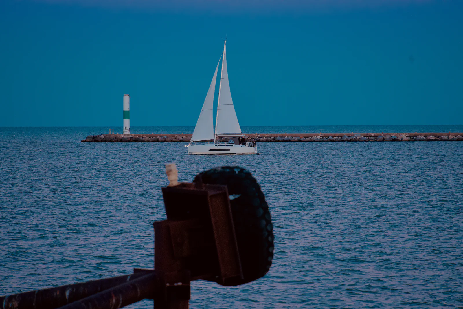 A white sailboat on blue water beyond the waterfront.