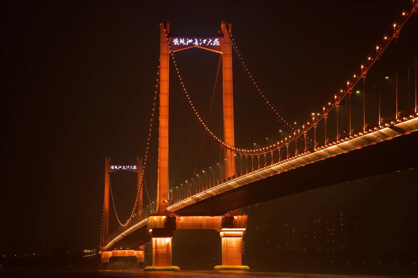 An illuminated suspension bridge spanning the river at night.