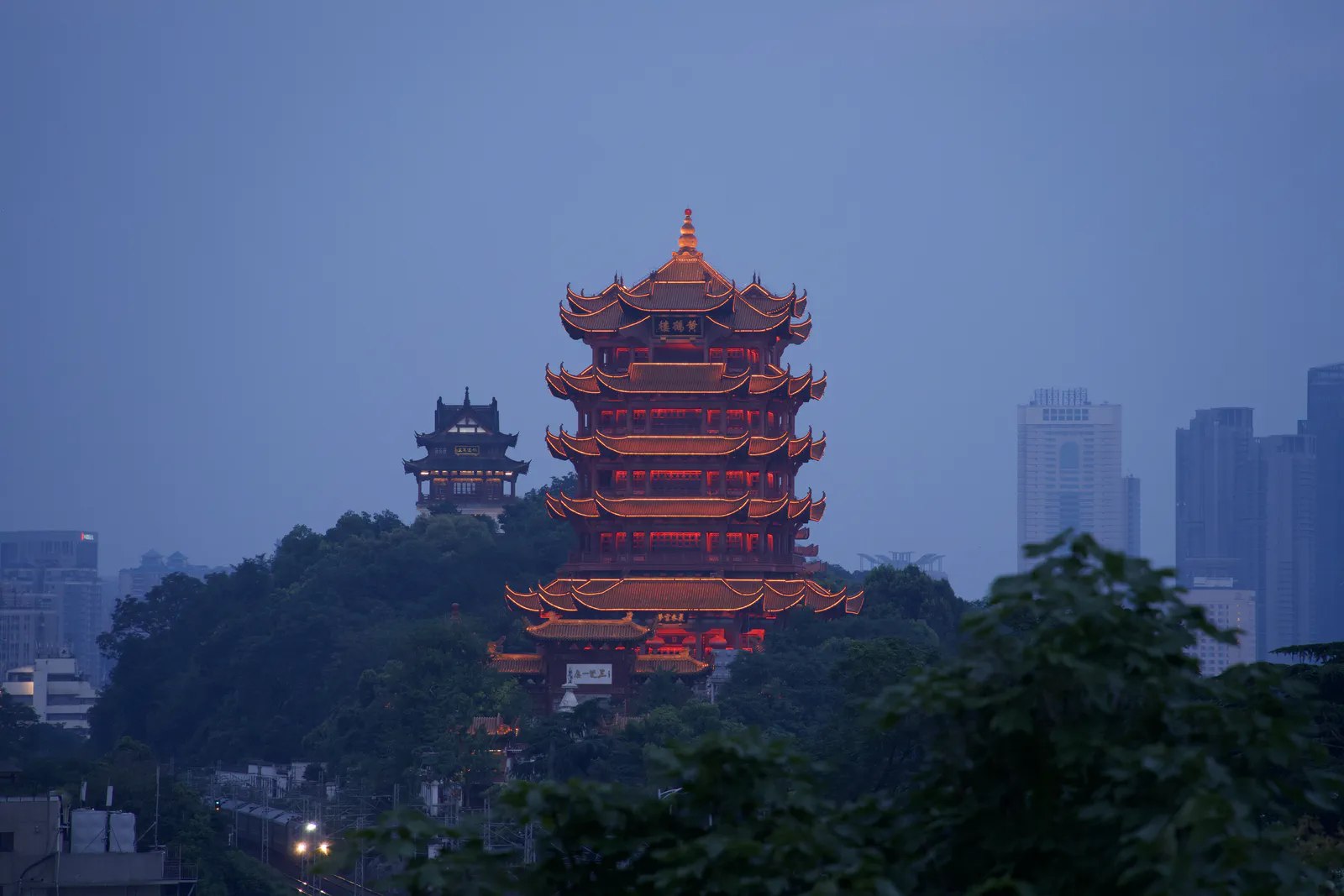 The illuminated Yellow Crane Tower rising above dark trees and the city.
