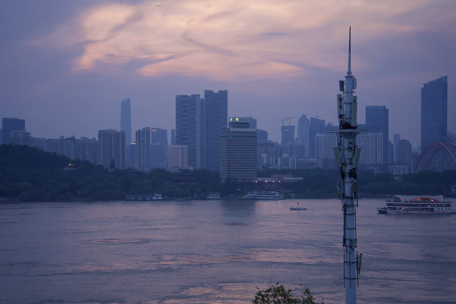 Riverside buildings and a foreground tower beneath layered sunset clouds.