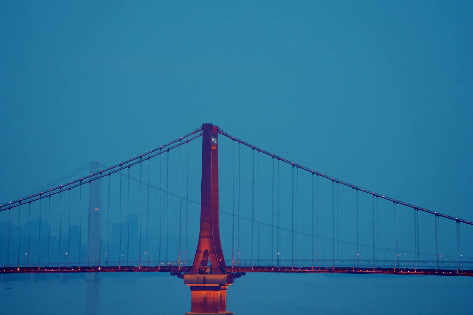 A red suspension bridge against a deep blue evening sky.