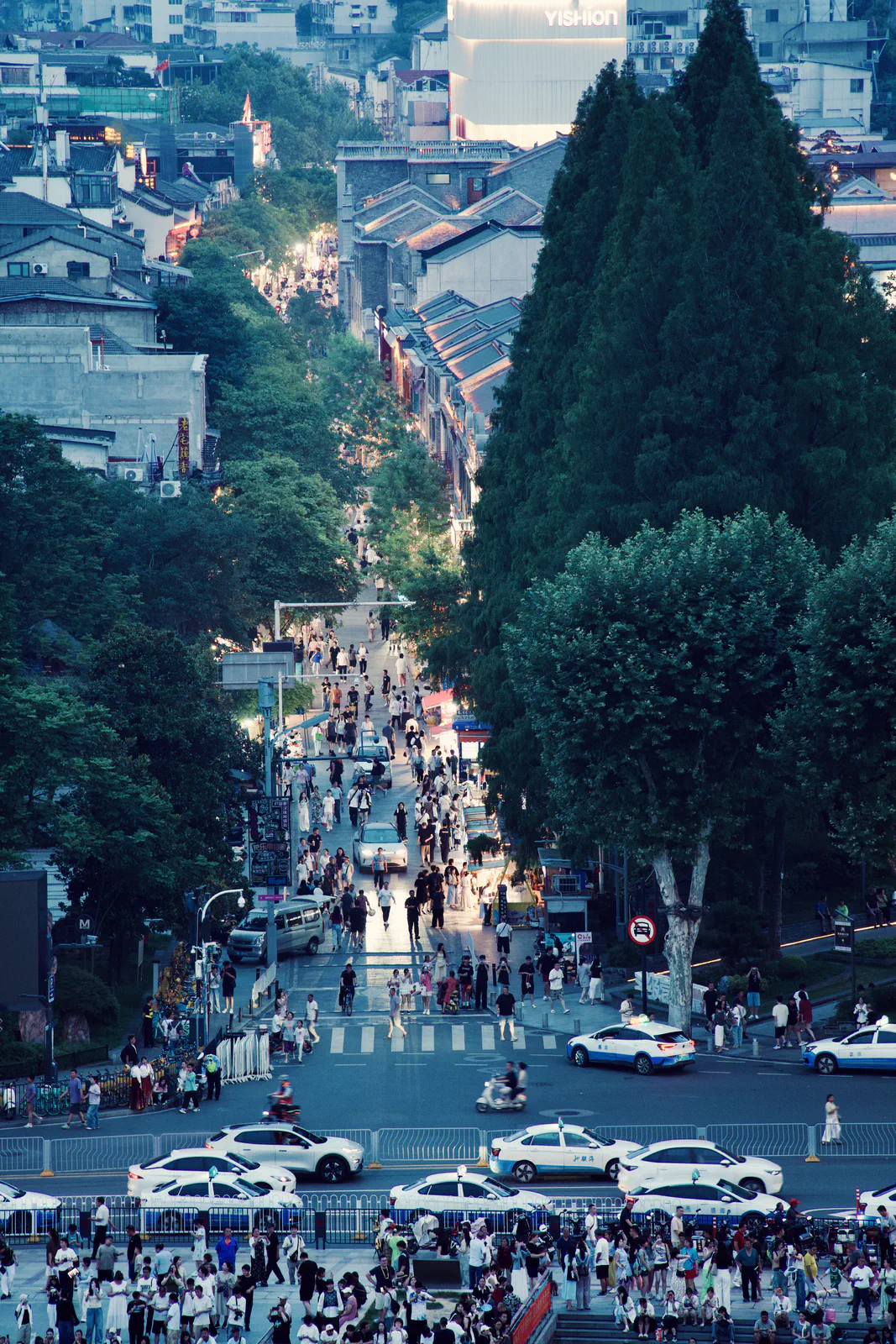 A busy tree-lined street leading toward an illuminated tower.