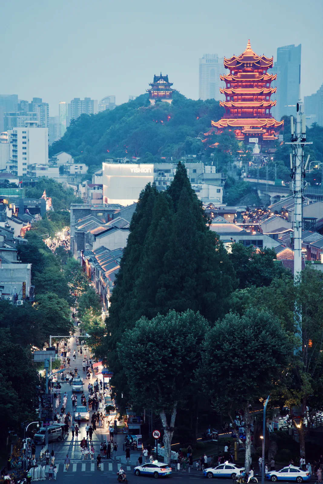 The Yellow Crane Tower overlooking a crowded street at dusk.