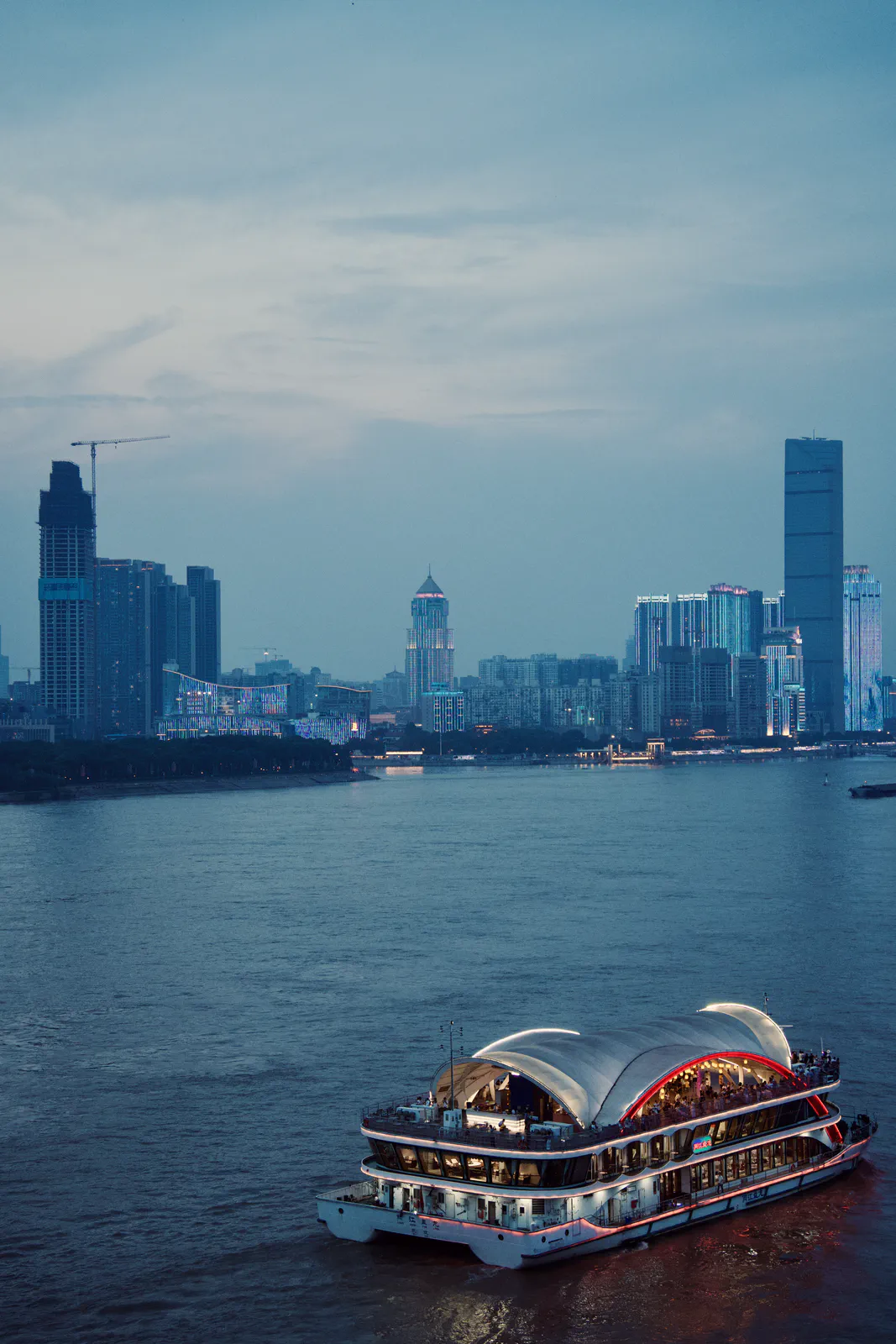 An illuminated sightseeing boat on the river below the city skyline.