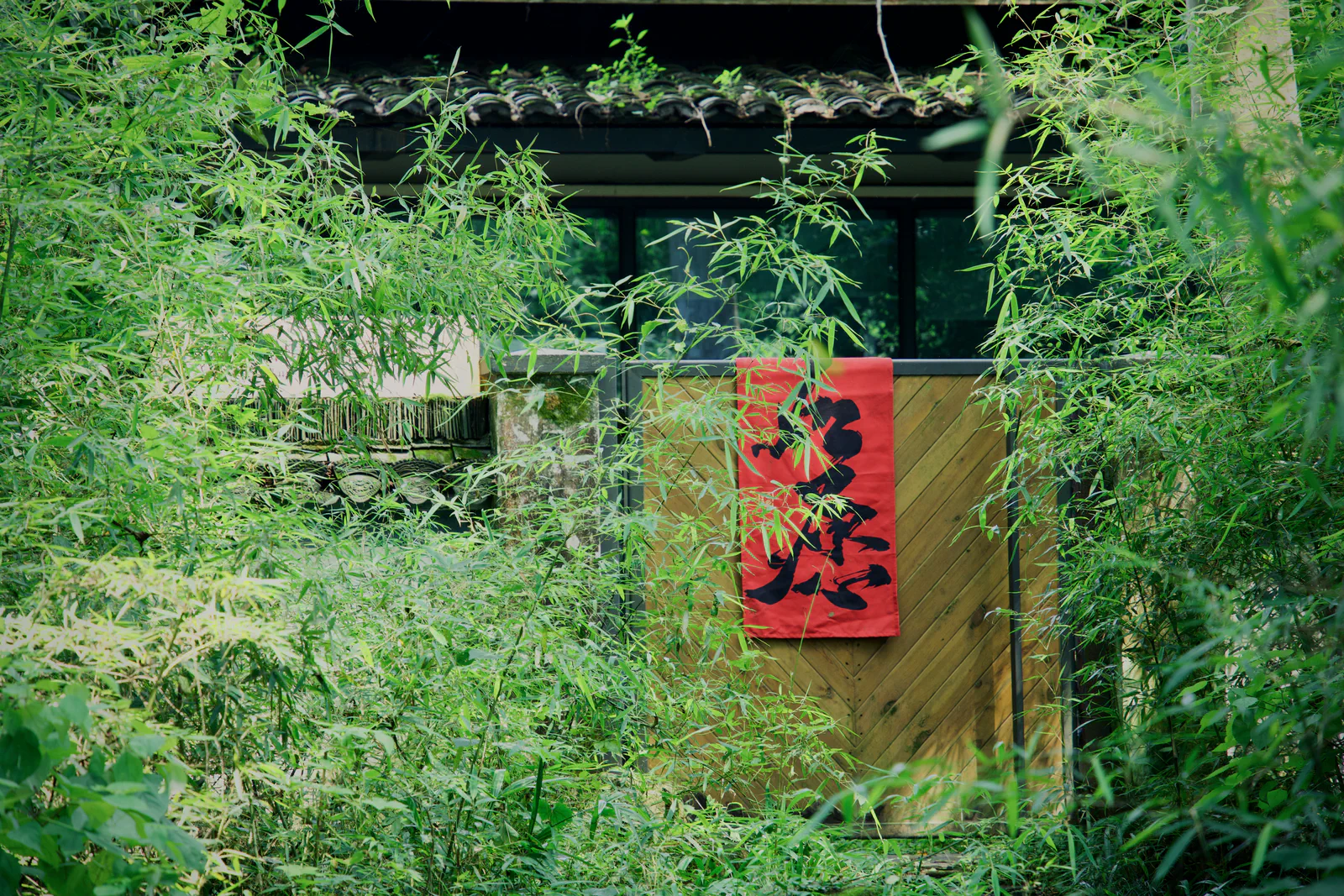 A red calligraphy banner on a bamboo wall surrounded by green foliage.